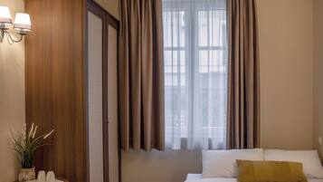 A hotel room with a bed, a nightstand, a lamp, a window with curtains, and a view of the outside.