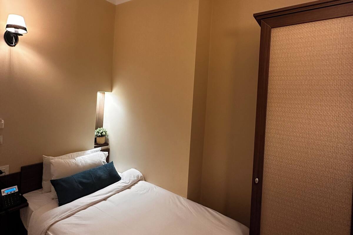 A hotel room with a bed, a nightstand, a lamp, and a door.