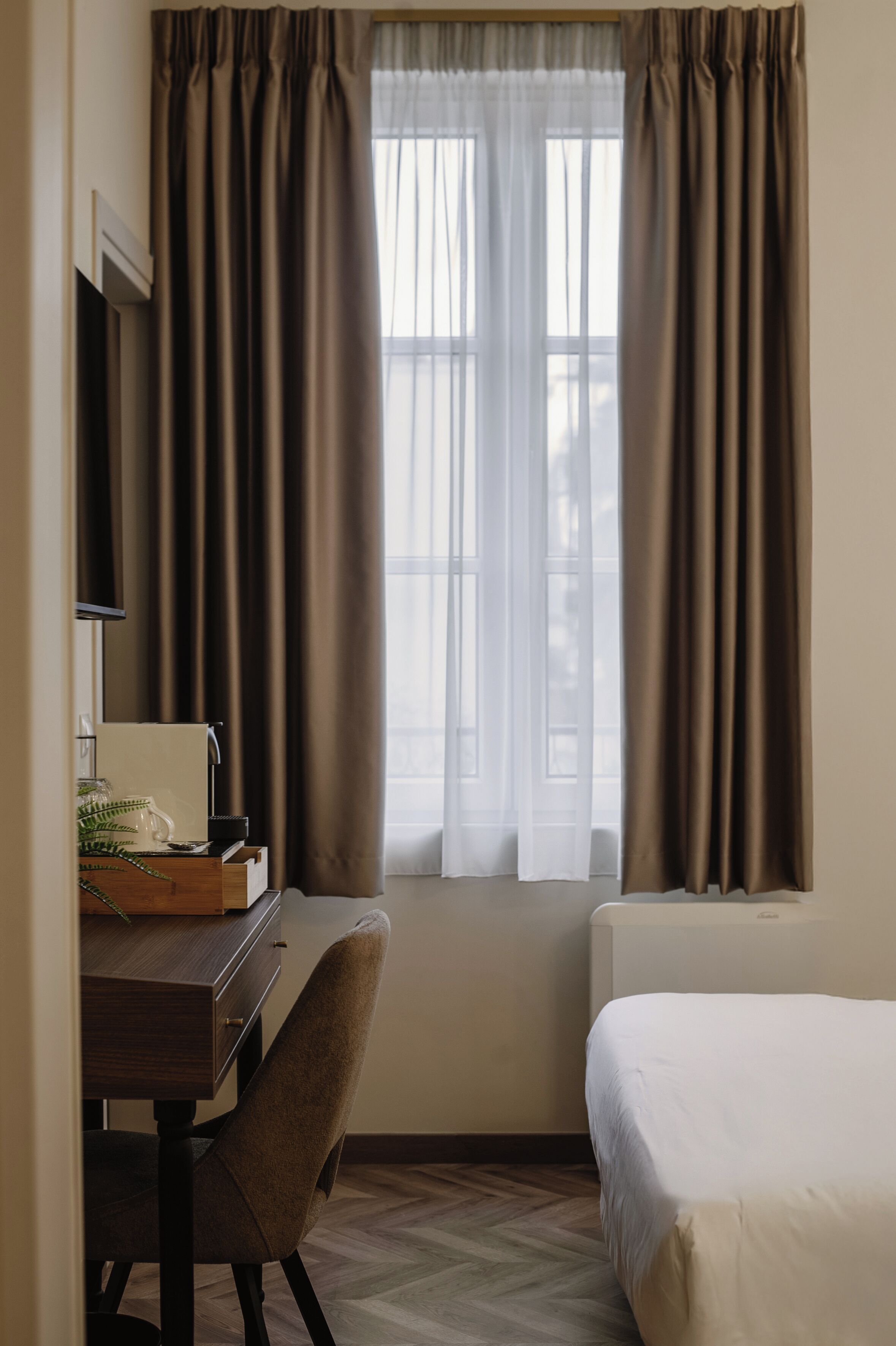 Una habitación de hotel con escritorio, silla, cama y ventana con cortinas.