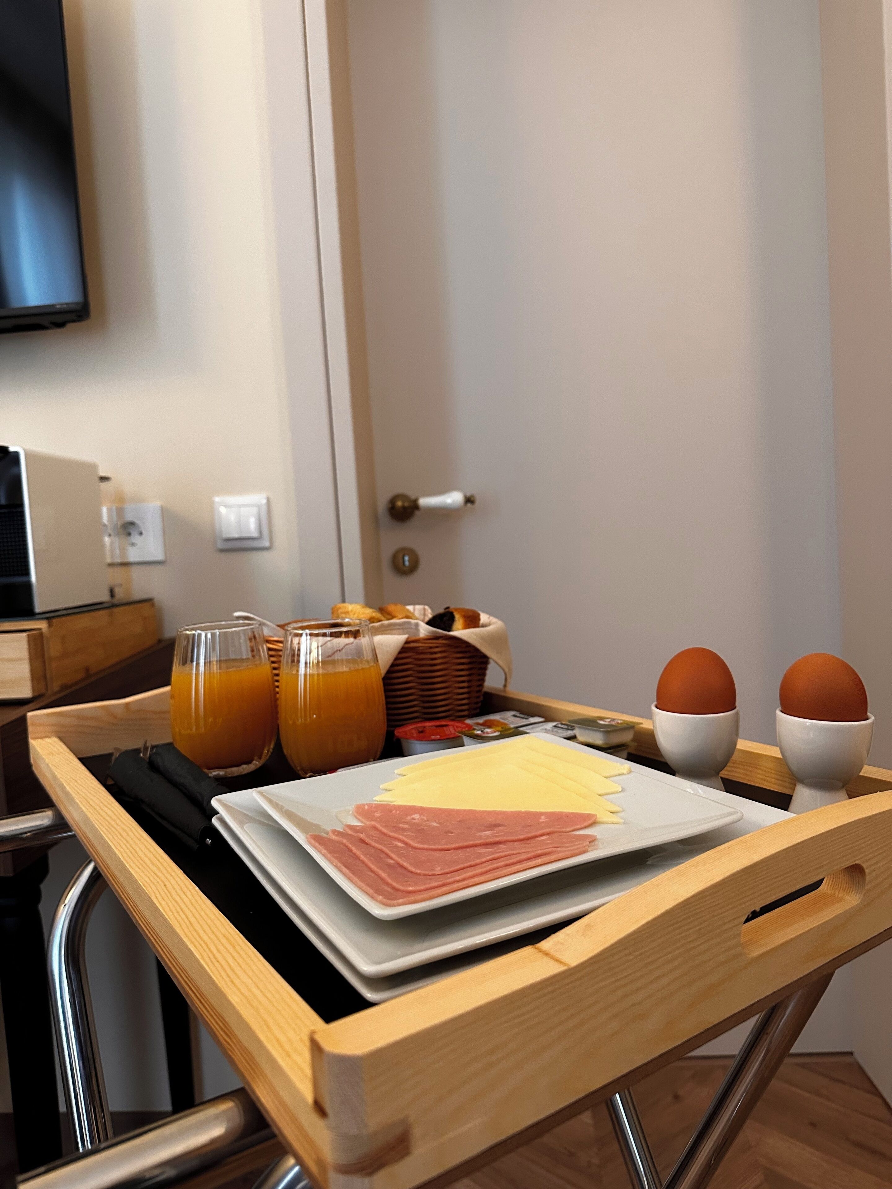 A breakfast tray with eggs, cheese, ham, and orange juice on a wooden table in a hotel room.