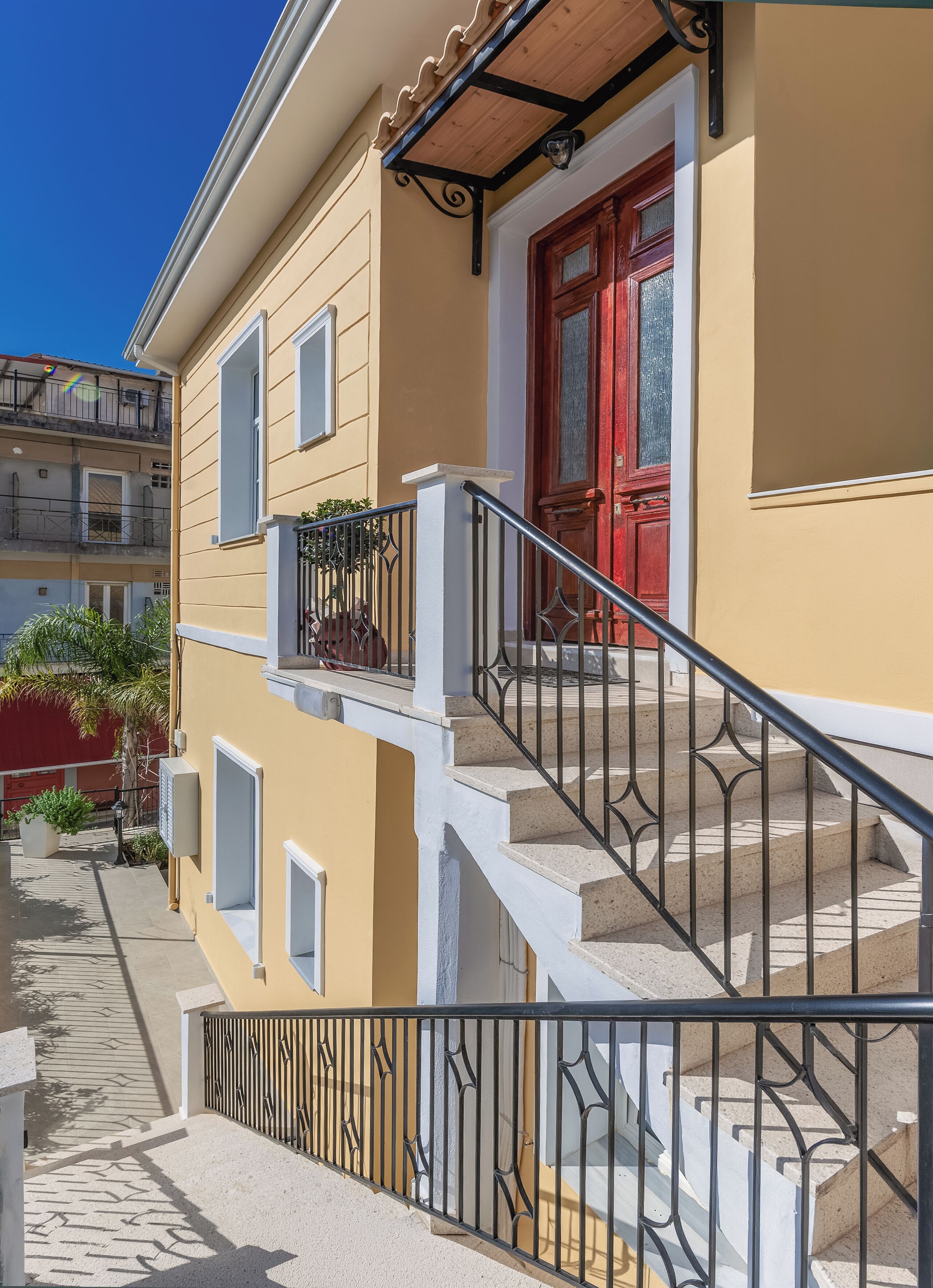 Un edificio de dos pisos con puerta roja, balcón y escalera.