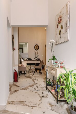 A room with a dining table, chairs, a potted plant, a fire extinguisher, and a wall-mounted artwork. - Maissance (Preveza)