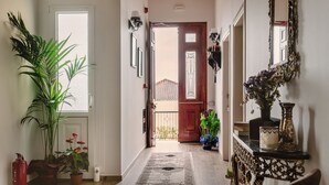 A hallway with a wooden floor, a patterned rug, potted plants, a fire extinguisher, and a mirror on the wall. - Maissance (Preveza)