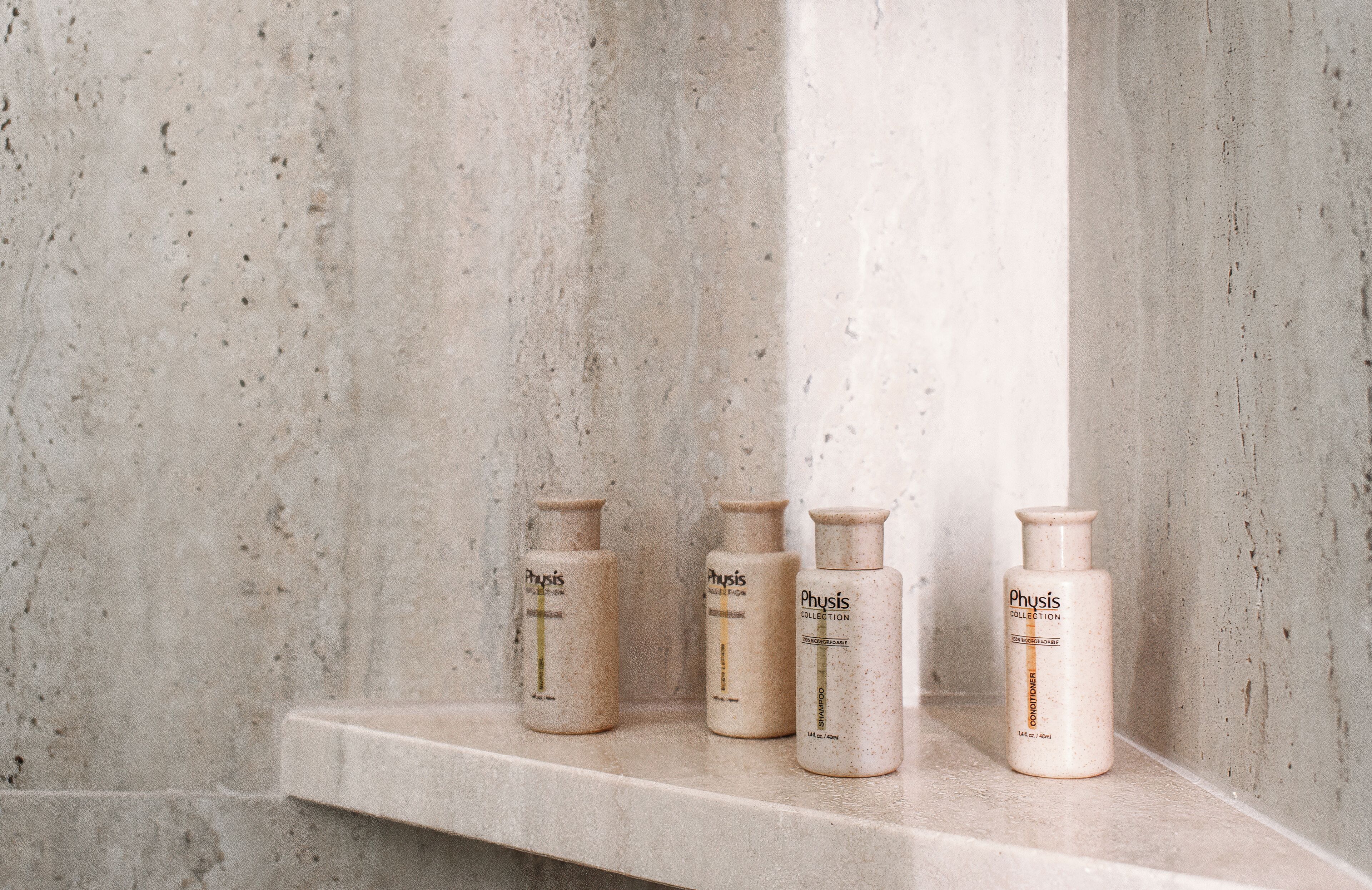 Three Physis Collection toiletry bottles on a marble shelf against a textured wall.