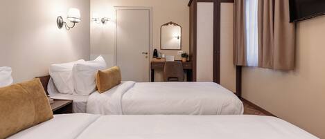A hotel room with two beds, a desk with a chair, a mirror, a television, and a window with curtains.