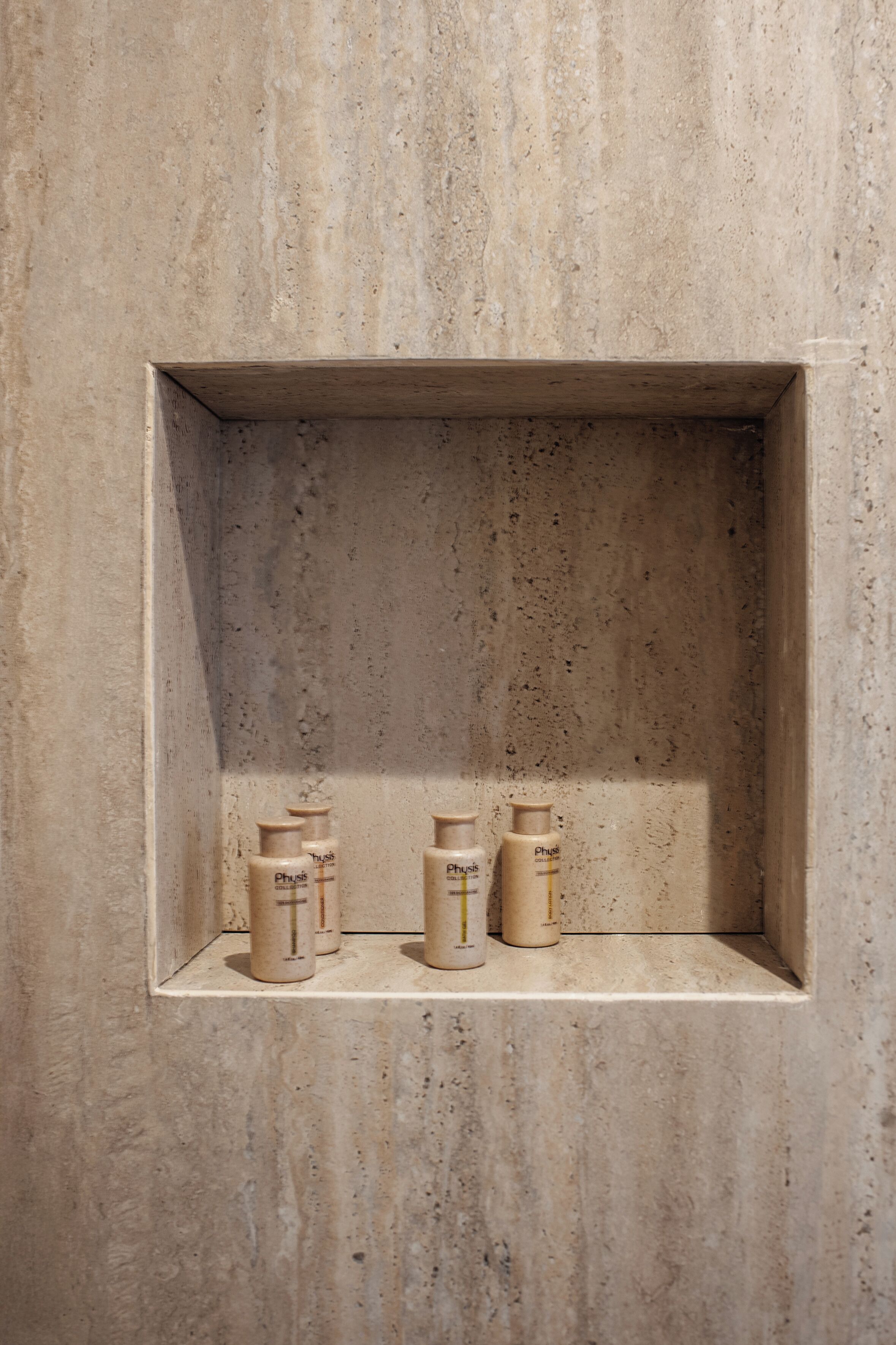 A bathroom with a textured wall and a shelf holding three toiletry bottles.