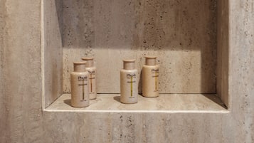 A bathroom with a textured wall and a shelf holding three toiletry bottles.