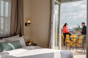 A hotel room with a bed, a nightstand, a lamp, and a balcony with a table and chairs. - Maissance (Preveza)
