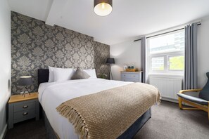 A bedroom with a large bed, a bedside table with a lamp, a chair, and a window with curtains. - Harbour Hub Hotel (Southampton)