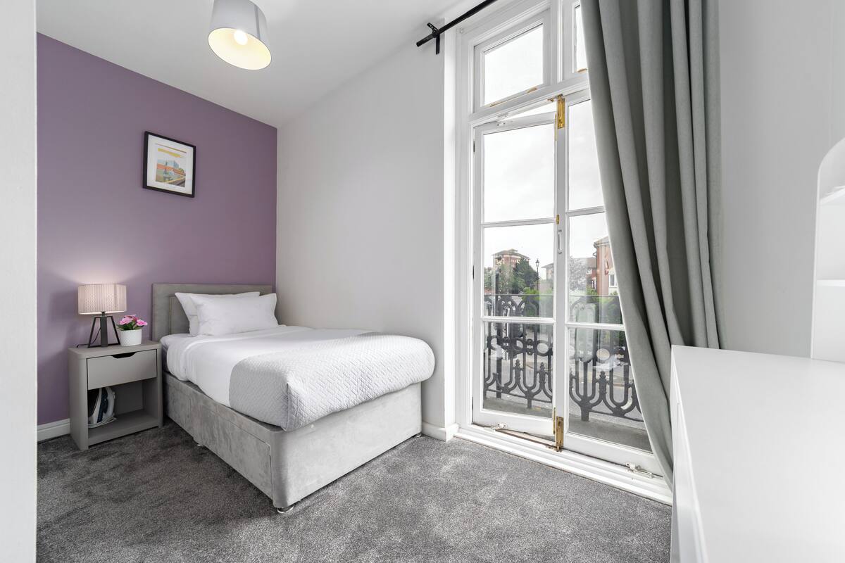 A bedroom with a bed, nightstand, lamp, and window with curtains.
