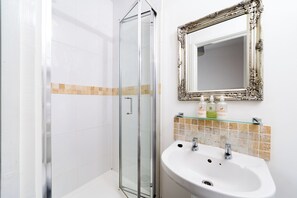 A bathroom with a glass shower enclosure, a white sink, and a mirror with an ornate frame. - Harbour Hub Hotel (Southampton)