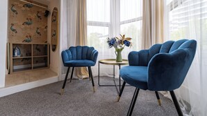 Ein Zimmer mit zwei blauen Sesseln, einem kleinen Tisch mit Blumenvase und einer dekorativen Wandverkleidung.