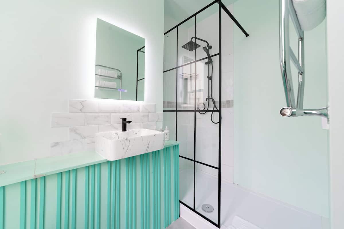 A modern bathroom with a glass-enclosed shower, a white marble sink, and teal-colored cabinetry.