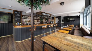 Eine Bar mit einer Holztheke, Barhocker und einem großen Fernsehbildschirm.