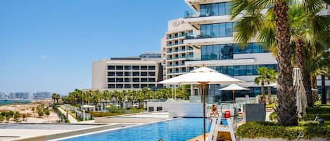 Une piscine d’hôtel offrant une vue dégagée sur la mer, des palmiers et un bâtiment moderne doté de balcons.