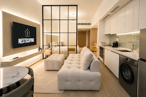 Un appartement moderne comprenant un salon, un canapé, un pouf, une cuisine et un téléviseur diffusant l'image « NESTSCAPING ».