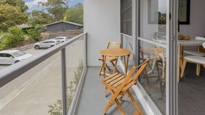 Un balcon avec des chaises et une table en bois, donnant sur un parking et des arbres.