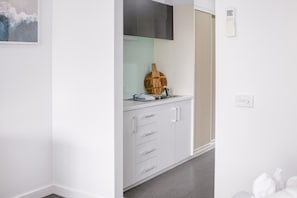 A modern kitchen with white cabinets, a wooden cutting board, and a stainless steel sink. - Bay View - The Trio Lorne (Lorne)