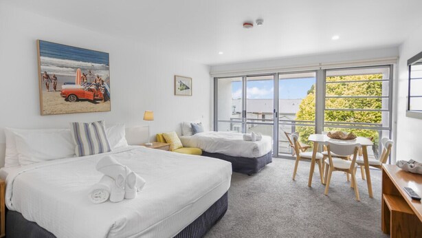 Une chambre d’hôtel avec deux lits, un balcon avec une table et des chaises, et une grande fenêtre donnant sur un paysage verdoyant.