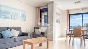 A modern living room with a grey sofa, a wooden coffee table, and a dining area with a wooden table and chairs. - CostaBlancaDreams - Apartment Turis in Calpe (Calpe)