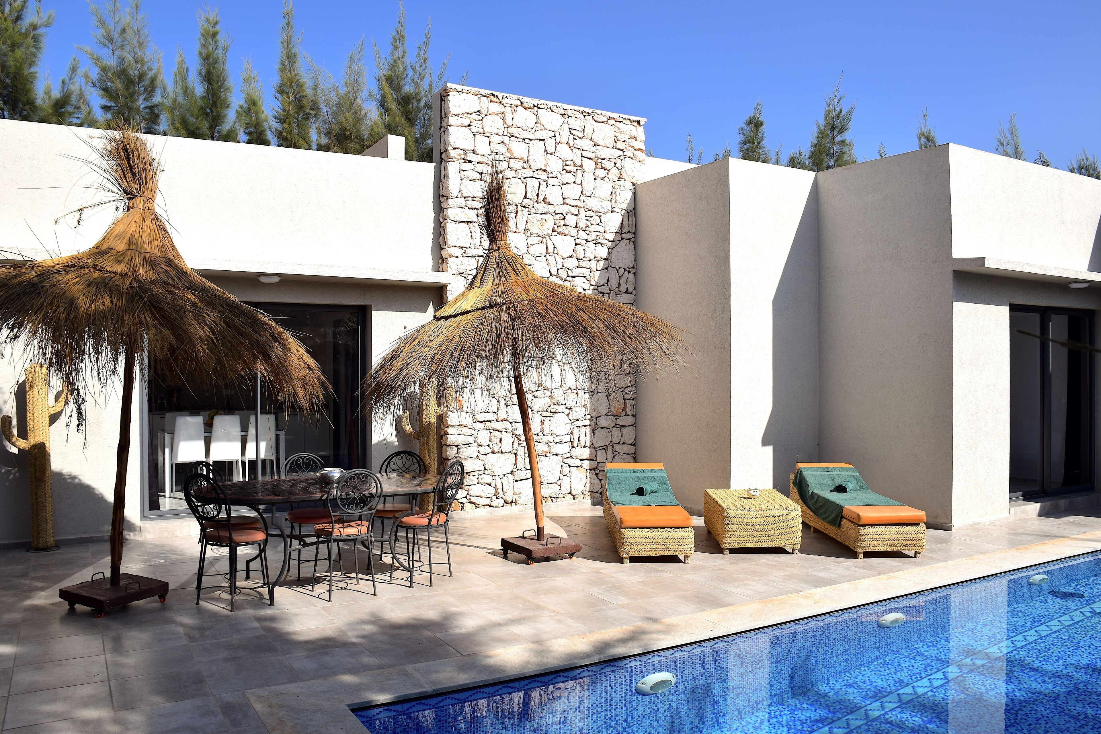 Un área de piscina exterior moderna con sillones reclinables, una mesa de comedor y un muro de piedra.