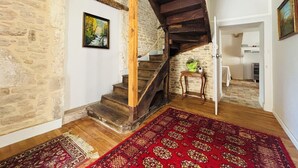 Un interno rustico con una scala in legno, pareti in pietra e un tappeto rosso decorato.
