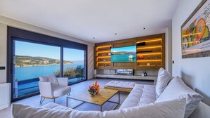 Uma sala de estar moderna com uma televisão grande, assentos confortáveis e uma vista panorâmica do mar.