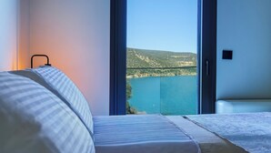 Quarto com uma janela ampla que oferece vista para um lago e colinas.