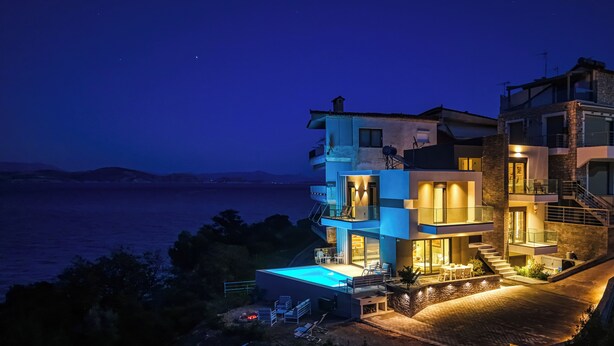Uma casa moderna de vários andares com piscina, área de estar externa e vista para o mar.