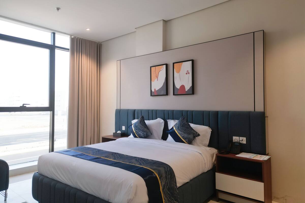 Quarto de hotel moderno com uma cama grande, mesa de cabeceira e uma janela ampla com vista para o exterior.