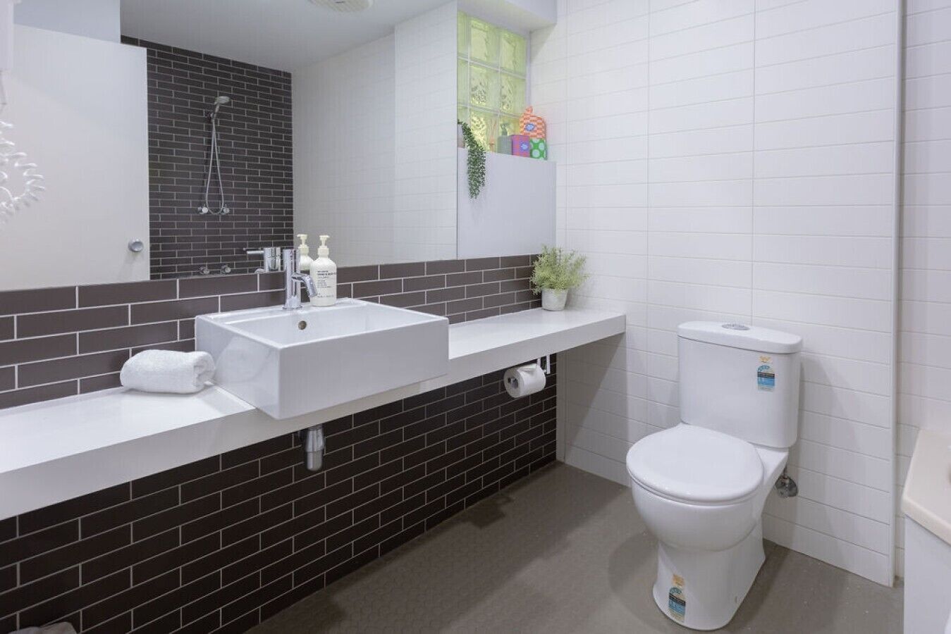 A modern bathroom with a white sink, black tiled backsplash, a toilet, and a shower.