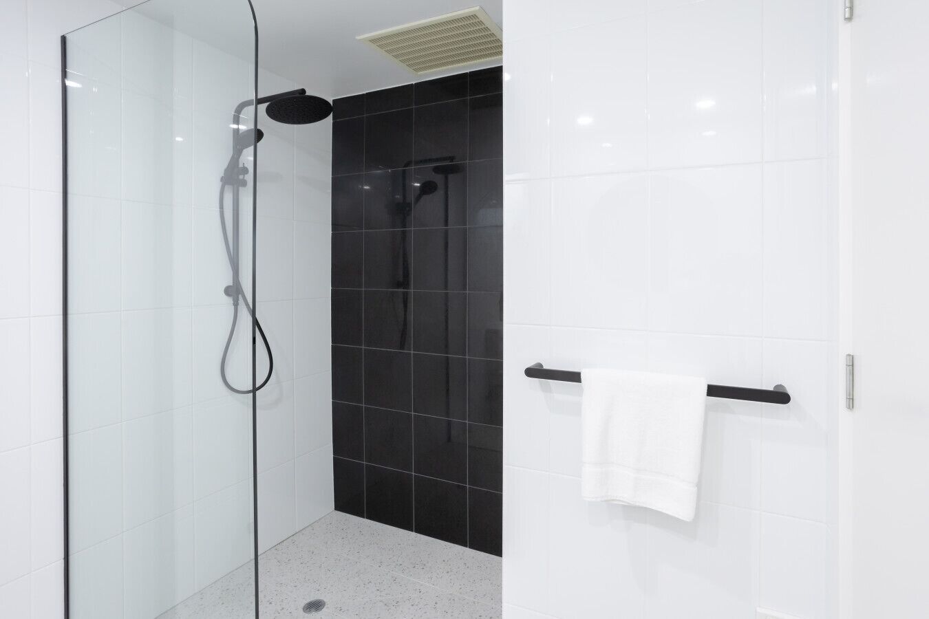 A modern shower with a glass door, a black tiled wall, and a white towel rack.