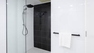 A modern shower with a glass door, a black tiled wall, and a white towel rack.