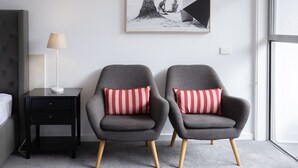 A modern room with two grey armchairs, a small bedside table with a lamp, and a framed picture on the wall. - Bay View: Breeze (Lorne)