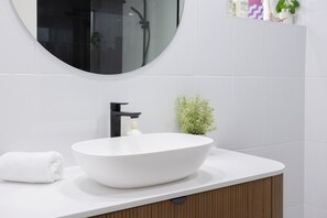 Une salle de bain avec un lavabo blanc, un robinet noir et un miroir au-dessus.