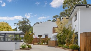 A modern building with a flat roof, a covered walkway, and a fenced garden area with various plants. - Bay View: Breeze (Lorne)