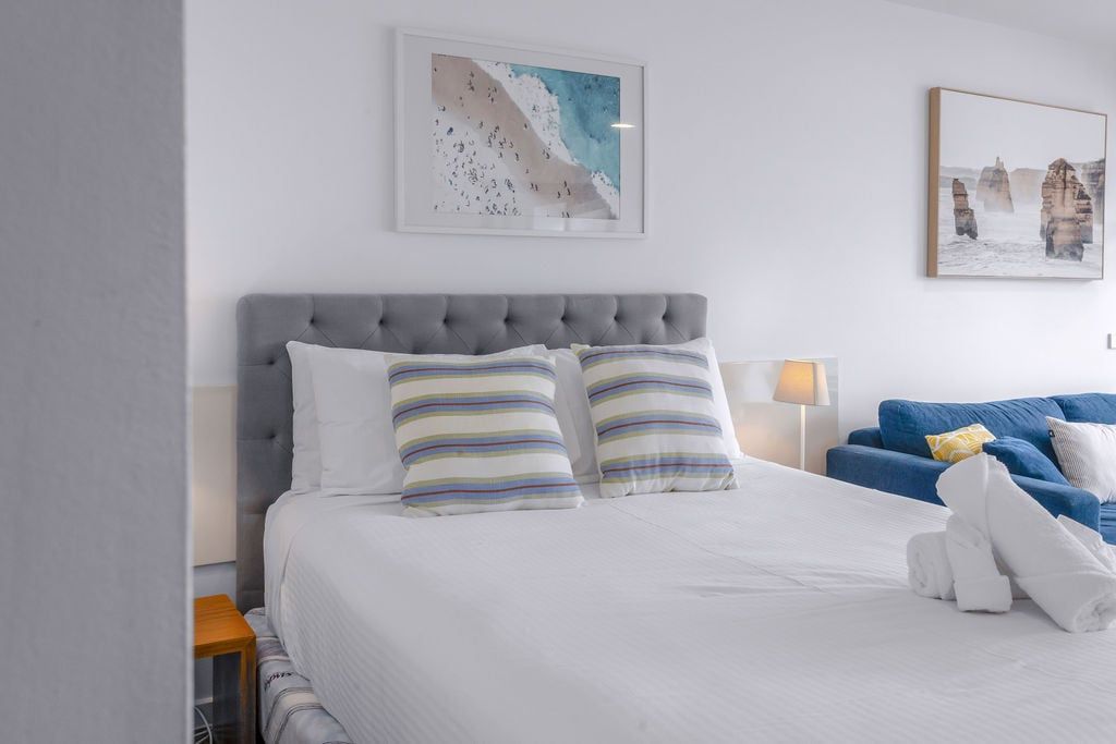 Una habitación de hotel con una cama grande, almohadas a rayas, un sofá azul y obras de arte en las paredes.