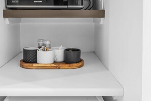 Une étagère de cuisine avec un four à micro-ondes, un plateau en bois avec des récipients et un plan de travail blanc.