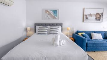 A hotel room with a bed, two bedside lamps, a blue sofa, and two wall-mounted artworks.
