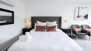 A hotel room with a large bed, two bedside tables, a wall-mounted air conditioner, a framed picture, and two armchairs. - Bay View: Sunrise (Lorne)