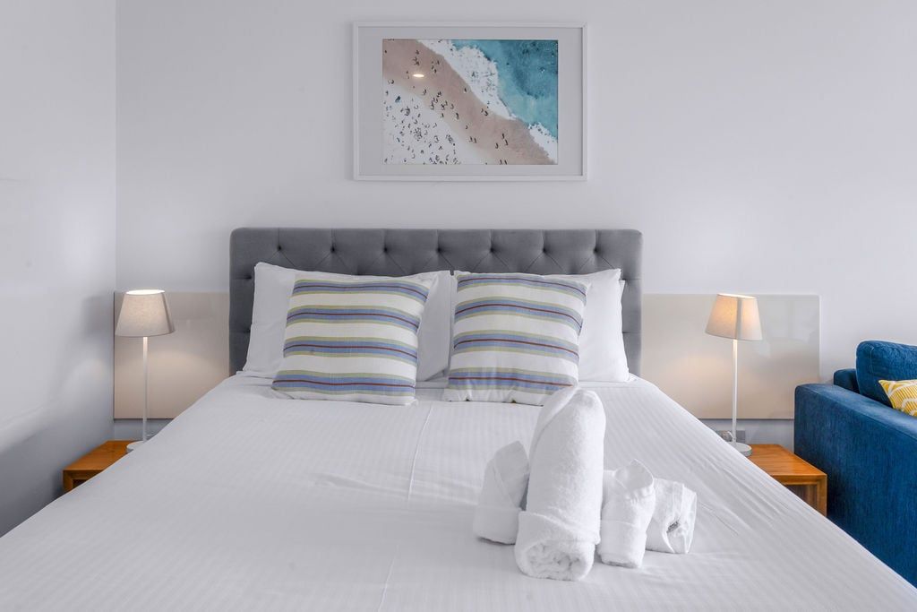 A neatly made bed with striped pillows, a grey upholstered headboard, and a framed artwork above.
