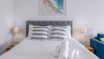 A neatly made bed with striped pillows, a grey upholstered headboard, and a framed artwork above.