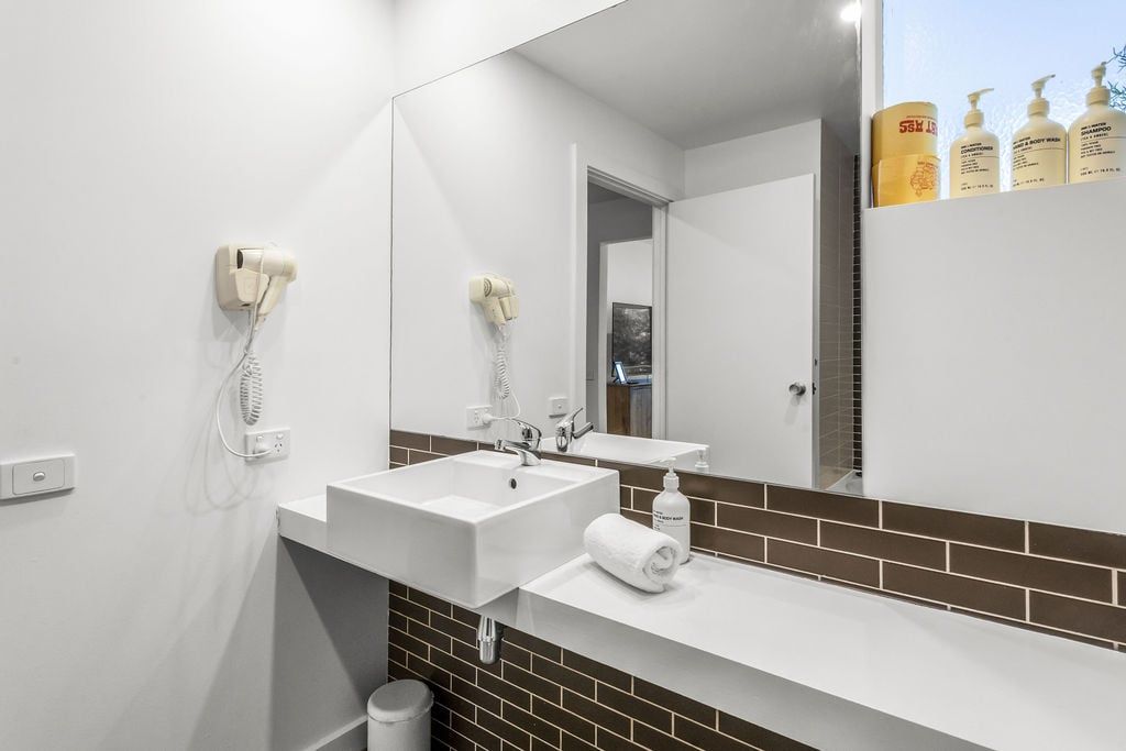A modern bathroom with a large mirror, two sinks, and a hairdryer mounted on the wall.