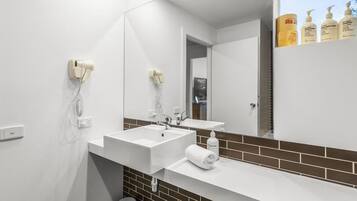 A modern bathroom with a large mirror, two sinks, and a hairdryer mounted on the wall.