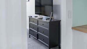 A black dresser with drawers, a flat-screen TV mounted above it, and a small plant on top. - Bay View: Sunrise (Lorne)