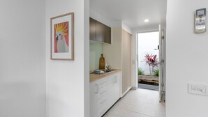 A modern kitchen with white cabinets, a wooden countertop, and a framed artwork on the wall. - Bay View: Sunrise (Lorne)