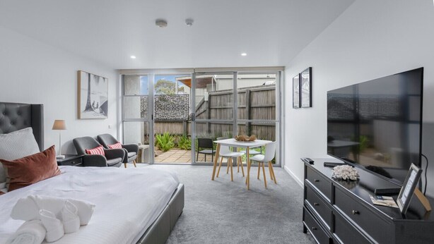 A modern bedroom with a bed, a desk, a TV, and a sliding glass door leading to an outdoor area. - Bay View: Sunrise (Lorne)