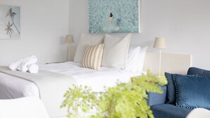 A hotel room with a bed, two bedside lamps, a painting of a person in water, and a blue sofa. - Bay View: Ocean Views (accessible) (Lorne)