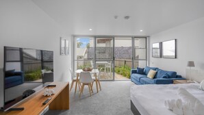 A modern hotel room with a bed, a TV, a desk, and a balcony with a view of the outside. - Bay View: Alfresco (Lorne)