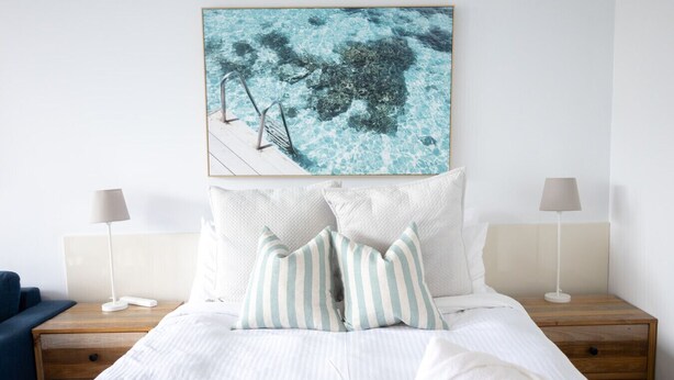 A neatly arranged bedroom with a bed, two bedside tables with lamps, and a large framed picture above the bed. - Bay View: Alfresco (Lorne)